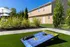 Inviting outdoor space with a cornhole game on a lush lawn, framed by vibrant greenery and modern apartments under a clear blue sky.