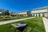 Inviting outdoor space with vibrant green lawn, cornhole games, picnic tables, and well-maintained landscaping under a clear blue sky.