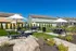 Charming outdoor communal space featuring lush landscaping, picnic tables with large umbrellas, and multiple BBQ grills, perfect for social gatherings in a serene atmosphere.