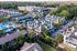 Aerial view of a modern apartment complex with lush greenery, spacious residences, a large swimming pool, and ample parking.