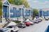 Charming blue apartment complex with modern architecture, featuring convenient parking and lush greenery under a clear sky.