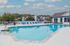 Inviting outdoor pool area with crystal-clear water, surrounded by blue loungers and scenic views of nearby residences.