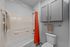 Modern bathroom featuring white tiles, vibrant orange shower curtain, and sleek gray cabinets for a stylish and functional space.