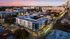 Vibrant aerial view of modern apartment complex at dusk, surrounded by a lively urban setting with stunning sunset skies.