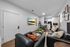 Modern living room featuring sleek black sofas, a stylish coffee table with greenery, a wall-mounted flat screen TV, and an elegant dining area by a cozy kitchen.
