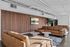 Contemporary apartment lounge with luxurious brown leather sofas, modern wood-paneled wall, stylish artwork, and lush indoor plant.