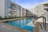 Modern apartment complex boasting a pristine outdoor swimming pool, stylish poolside seating, and elegant balconies under a clear blue sky.