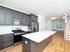 Contemporary open-concept kitchen with sleek grey cabinetry, stainless steel appliances, and elegant wood flooring leading to a bright living area.