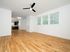 Spacious living area with modern hardwood floors, ample natural light through large windows, and a sleek, open kitchen in the background.