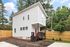 Modern two-story home with sleek white siding, charming red door, and inviting front porch nestled in a serene, tree-lined neighborhood.