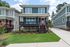 Charming two-story house with a vibrant red door, spacious balcony, and lush green lawn in a serene neighborhood.