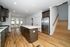 Modern kitchen with sleek stainless steel appliances, elegant dark cabinetry, and a spacious island. Open layout leads to a bright living area with large windows and wooden flooring.