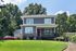 Modern two-story grey house with a welcoming porch and vibrant red front door, surrounded by lush greenery and a spacious lawn.
