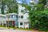 Charming modern two-story home with large windows, surrounded by lush greenery in a serene neighborhood setting.