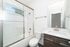 Elegant modern bathroom showcasing a chic glass-enclosed bathtub, sleek vanity, and bright natural lighting.