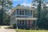 Charming two-story house with blue siding and a vibrant red door, nestled among trees with a welcoming front porch and driveway.