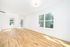 Bright and airy living room with elegant hardwood floors, large windows, and modern lighting, offering a serene view of greenery.