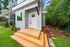 Charming modern townhouse with inviting wooden steps, lush greenery, and a serene forest path.