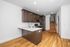 Modern kitchen with sleek dark cabinets, stainless steel appliances, and elegant hardwood floors, leading to a graceful staircase.