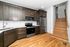 Sleek modern kitchen with stainless steel appliances, elegant dark wood cabinetry, and inviting wooden stairs leading to the upper level.