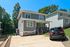 Charming two-story gray house with a welcoming porch and spacious driveway, nestled in a lush, green neighborhood.