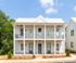 Charming two-story apartment with modern colonial design, featuring a welcoming balcony and lush surroundings under a clear blue sky.