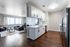 Modern open-concept living space featuring a sleek kitchen with white cabinetry, hardwood floors, and a cozy living area with abundant natural light.