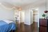 Inviting bedroom with sleek hardwood floors, cozy string lights, and adjoining walk-in closet, featuring a glimpse into a modern kitchen.