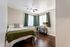 Cozy bedroom featuring a comfortable bed with green accents, elegant hardwood floors, and a stylish desk by the window with green curtains.