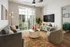 Bright and cozy living room with modern decor, featuring a plush grey sofa, vibrant patterned rug, large flat-screen TV, and floor-to-ceiling windows opening to a lush garden view.