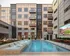 Modern apartment complex courtyard featuring a luxurious pool, sun loungers, and an outdoor seating area with a large screen.