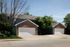 Charming duplex with brick accents and two spacious garages, nestled in a serene suburban neighborhood surrounded by lush greenery.
