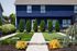 Charming blue two-story house with lush landscaping, welcoming pathway, and vibrant greenery.