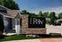 Inviting entrance sign of 'The Row' apartment complex, featuring modern stone accents and lush greenery under a clear blue sky.
