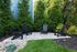 Charming outdoor space with four elegant black chairs on a stone patio, surrounded by lush greenery and vibrant trees.