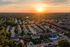 Scenic aerial view of a charming residential neighborhood during a vibrant sunset, showcasing tree-lined streets and rows of cozy homes with a lush green backdrop.