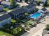 Aerial view of a modern apartment complex featuring lush green landscapes, a stylish outdoor pool area with sun loungers, and a cozy garden space with hammocks and seating, ideal for relaxation and community living.