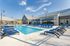 Luxurious outdoor pool area with stylish blue lounge chairs and a modern clubhouse under a bright, sunny sky.