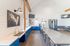Modern communal kitchen with striking blue cabinets, expansive countertops, and high ceilings. Features sleek metallic stools and contemporary art, perfect for gatherings and events.