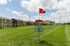 Vibrant residential area with colorful townhouses adjacent to a sprawling green disc golf course under a clear sky.