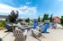 Charming outdoor patio area with colorful chairs, a cozy fire pit, and grill stations set against a backdrop of modern townhouses and vibrant blue skies.