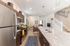 Modern open-plan kitchen and living area featuring sleek stainless steel appliances, elegant dark wood cabinetry, and a spacious granite island, leading to a cozy living room and staircase.