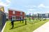 Modern outdoor fitness area with vibrant green artificial grass, surrounded by colorful houses and clear blue skies.