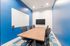 Modern conference room with vibrant blue accents, sleek wooden table, ergonomic chairs, whiteboard, and a wall-mounted screen.