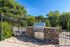 Inviting outdoor patio with a sleek built-in stone BBQ grill and a cozy seating area, surrounded by lush greenery.