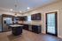 Modern kitchen with sleek dark cabinetry, granite countertops, stainless steel appliances, and a central island on polished wooden floors.