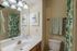 Charming bathroom with a nature-inspired theme, featuring elegant lighting, a floral shower curtain, and tasteful artwork.