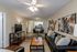 Inviting living room with elegant decor, cozy black leather sofas, modern ceiling fan, and bright open layout leading to a chic kitchen.