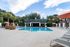 Inviting outdoor pool area featuring elegant loungers, tropical greenery, and a charming pavilion under a bright blue sky.