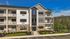Modern three-story apartment building with a stone and siding exterior, featuring private balconies and surrounded by lush greenery and vibrant landscaping.